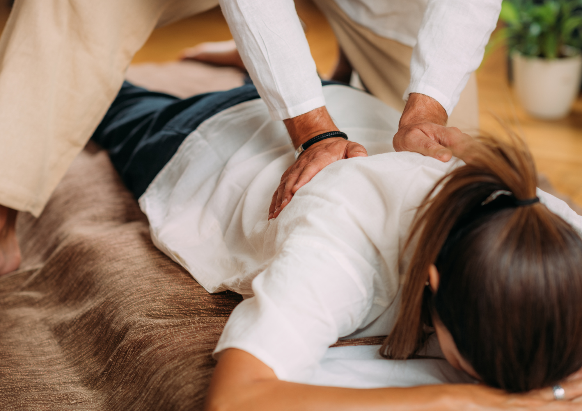 Praticien effectuant un massage relaxant du dos sur une femme allongée en tenue blanche