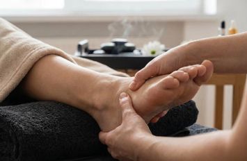 Praticien effectuant un massage relaxant des pieds et chevilles sur une personne allongée dans un espace de bien-être