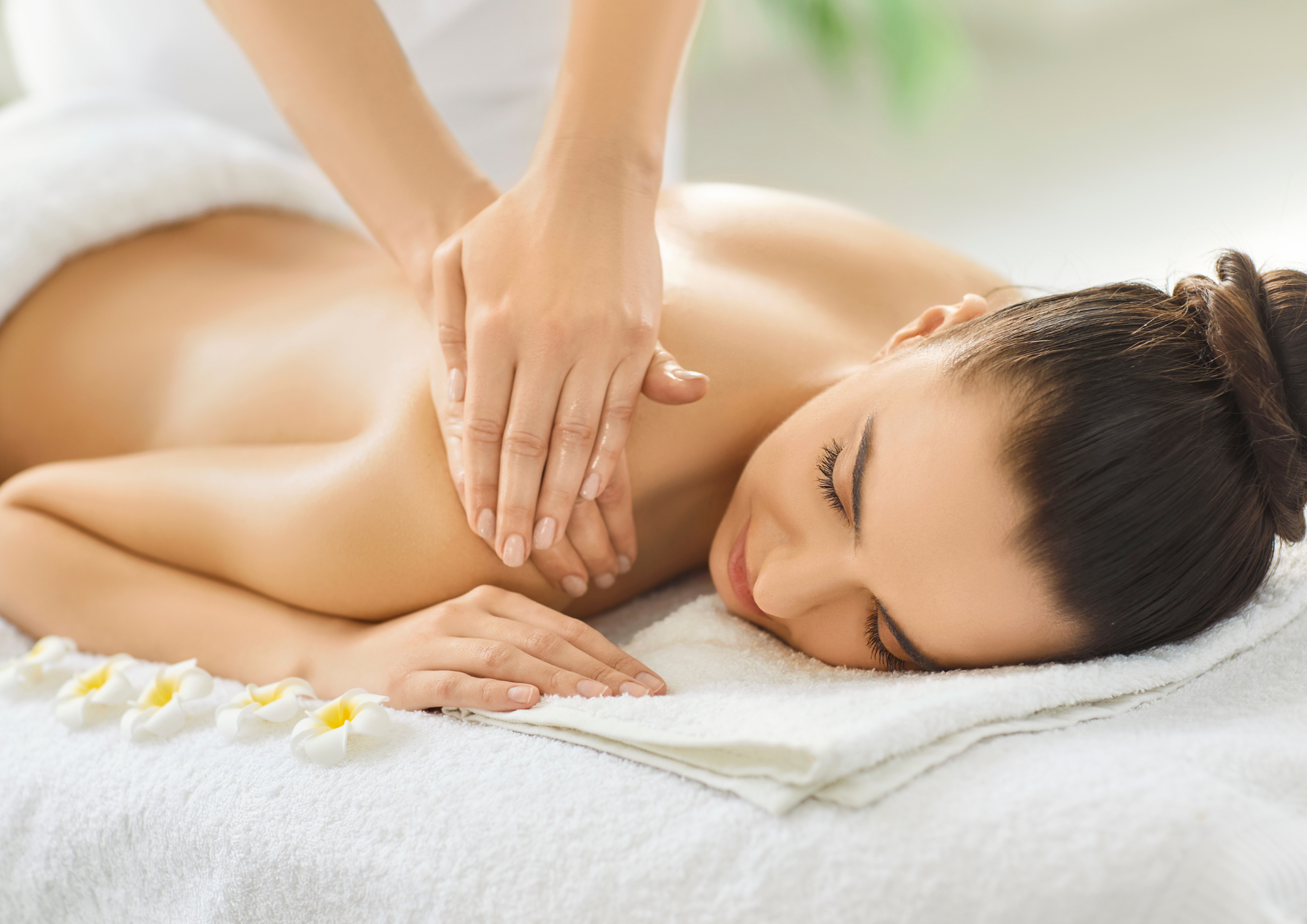 Femme recevant un massage relaxant du dos et des épaules par une thérapeute dans un environnement spa apaisant avec fleurs