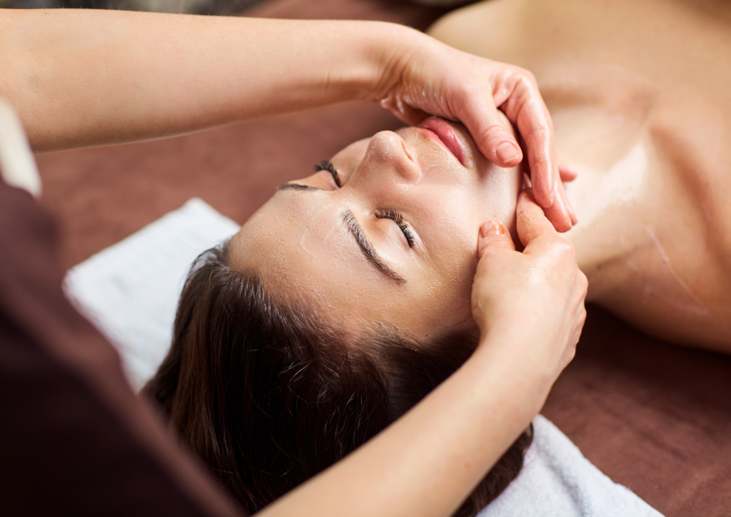 Praticienne effectuant un massage relaxant du visage et du cou sur une cliente allongée