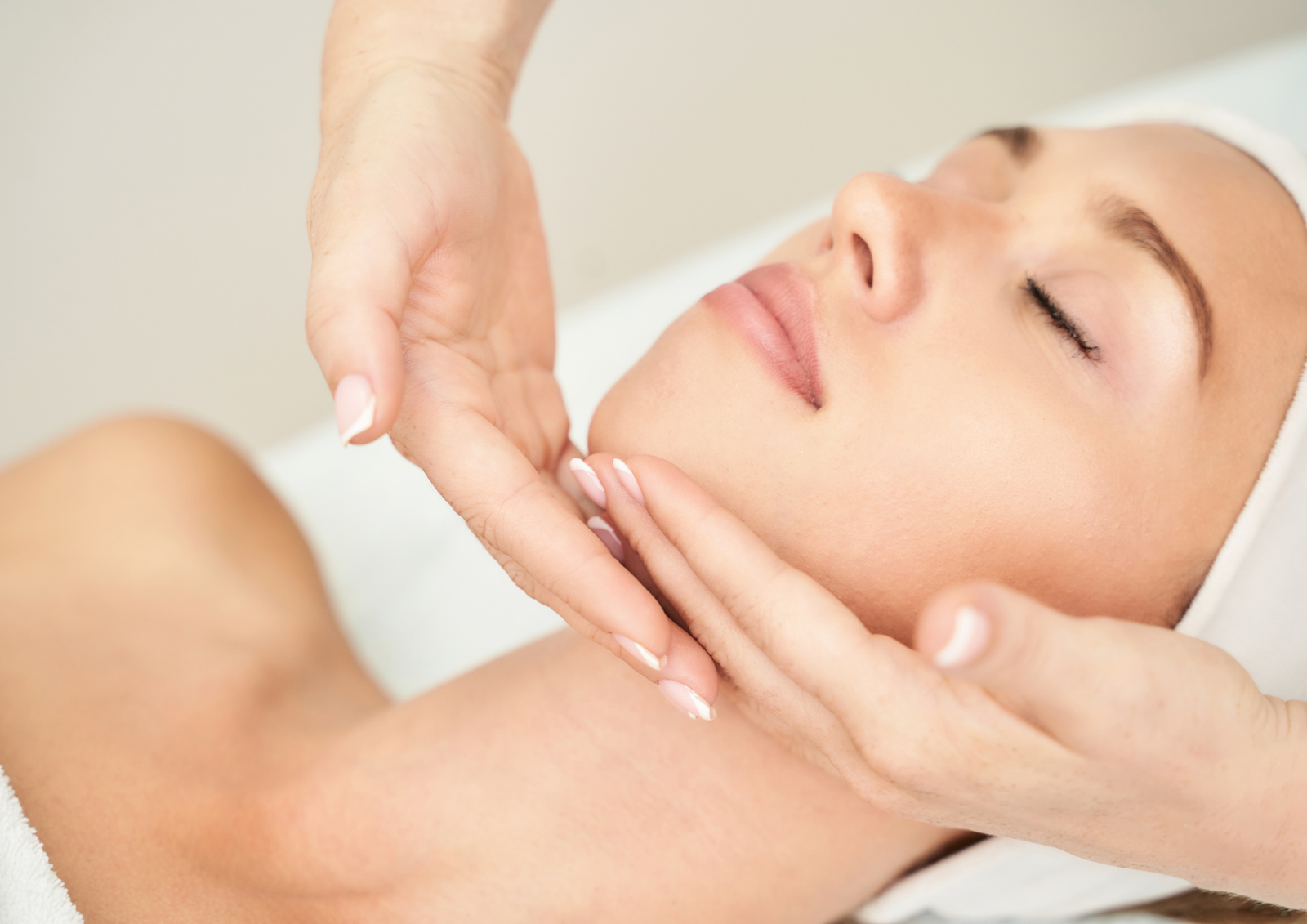 Praticien effectuant un massage facial relaxant sur une femme allongée avec les yeux fermés